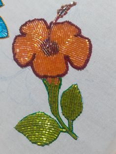 an orange flower with green leaves is on a white surface and blue butterflies are in the background