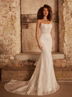 a woman in a white wedding dress standing next to a stone wall with an open doorway