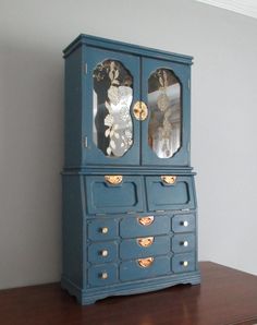 a blue cabinet with two mirrors on it's front and back doors, sitting on top of a wooden table