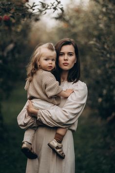 a woman holding a small child in her arms while standing next to an apple tree