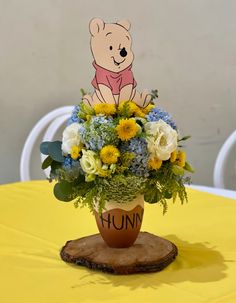 a winnie the pooh vase with flowers and greenery sits on a yellow tablecloth