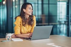 a woman sitting at a table with a laptop computer in front of her, smiling