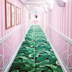 a long hallway with pink walls and green leaves on the floor in an art deco style