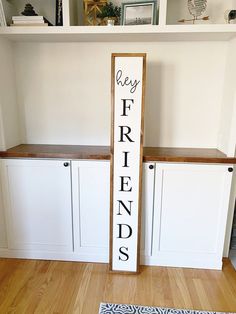 a wooden sign sitting on top of a hard wood floor next to white cupboards