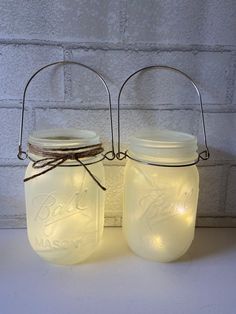 two mason jars with lights in them sitting on a table