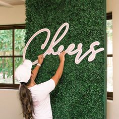 a woman is painting the letters on a green wall with fake grass behind her and another person standing next to it