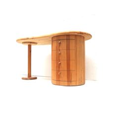 a wooden table with a circular top and two legs on the bottom, against a white wall