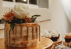 there is a cake with icing and flowers on the top, next to cupcakes