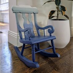 a blue rocking chair sitting on top of a hard wood floor next to a potted plant