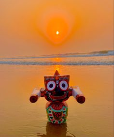 a statue sitting on top of a beach next to the ocean at sun rise in the sky