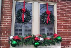 two christmas wreaths on the window sill with red and green ornaments hanging from them