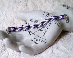 a purple and white beaded bracelet sitting on top of a hand with writing on it