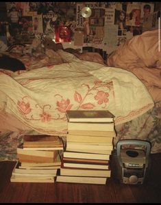 a pile of books sitting on top of a bed next to a phone and alarm clock