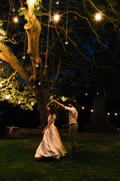 a man and woman dancing under a tree with lights hanging from it's branches