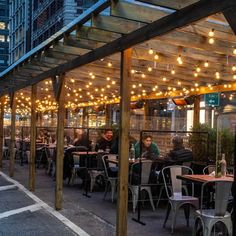 people are sitting at tables under an awning with lights strung from it's sides