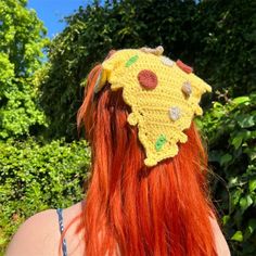 a woman with long red hair wearing a crocheted hat in the shape of a sunflower