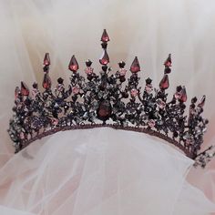 a tiara with pink and purple stones on it sitting on a white cloth covered surface