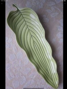 a green leaf shaped dish sitting on top of a white tablecloth covered wallpaper