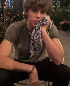 a young man is sitting on a chair and holding his hand to his face while wearing a scarf