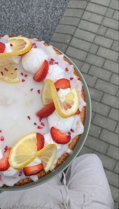 a person holding a cake with lemons and strawberries on it