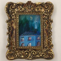 an ornate gold frame holds a painting of a blue house