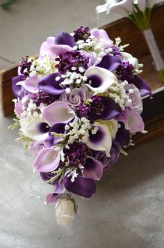 a bridal bouquet with purple and white flowers on the floor next to a wooden bench