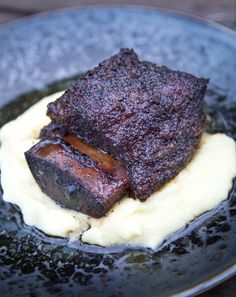 a piece of meat on mashed potatoes in a black plate with sauce and gravy