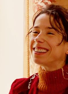 a woman smiling and wearing a red sweater