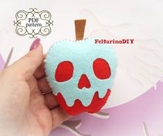 a hand holding an apple shaped brooch with a red and blue skull on it