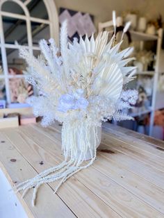 an arrangement of white flowers and feathers on a wooden table in front of a mirror