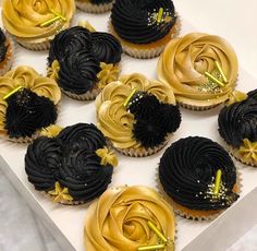 cupcakes decorated with gold and black icing in a box on a table