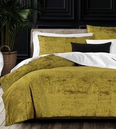 a bed with yellow and white comforters in a dark room next to a potted plant