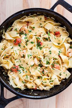 a skillet filled with pasta and shrimp on top of a wooden table