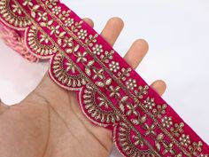 a hand is holding a piece of pink fabric with gold trimmings on it