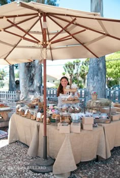 a woman is standing under an umbrella selling food at a table with bags on it