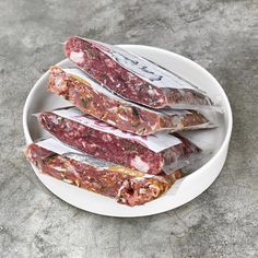 three raw meats on a white plate with silver foil wrapped in plastic wrappers