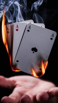 two hands holding playing cards with flames coming out of the top and on to them