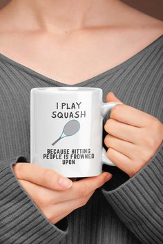 a woman is holding a coffee mug with the words, i play squash because hitting people is throwing them up