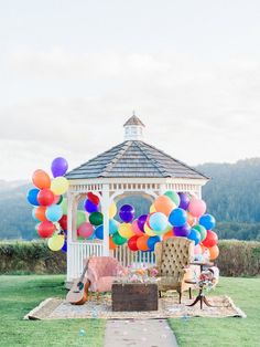 a gazebo with lots of balloons in the air and a couch on the grass