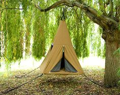 a teepee in the middle of a forest with trees and leaves around it, under a willow tree