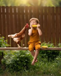 a little boy sitting on top of a wooden bench next to a chicken eating from a bowl