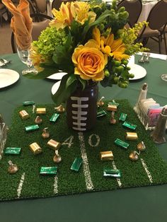 a football themed centerpiece is displayed on a green table cloth with flowers and candy