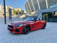 a red bmw z4 roadster parked in front of a large building with stairs leading up to it