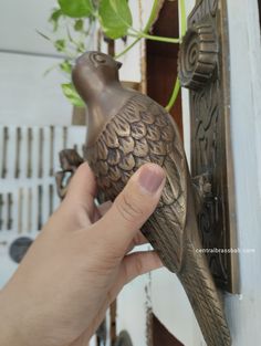 a hand is holding a bronze bird figurine in front of a wall mounted planter