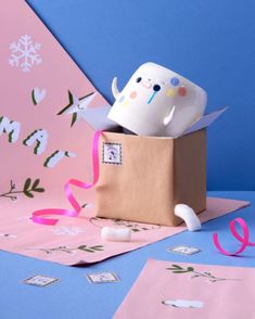 two cups in a cardboard box with streamers on the floor and snowflakes around them