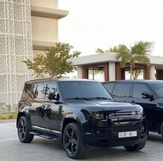 two black suvs parked next to each other in front of a building with palm trees