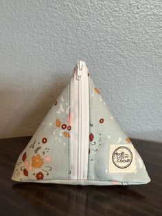 a small triangle shaped pouch with flowers on it sitting on a table next to a wall