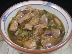 a bowl filled with meat and vegetables on top of a white cloth covered tablecloth