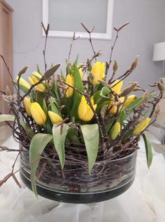 a glass bowl filled with yellow flowers on top of a white cloth covered tablecloth