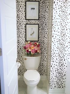 a white toilet sitting in a bathroom next to a wall with pictures and flowers on it